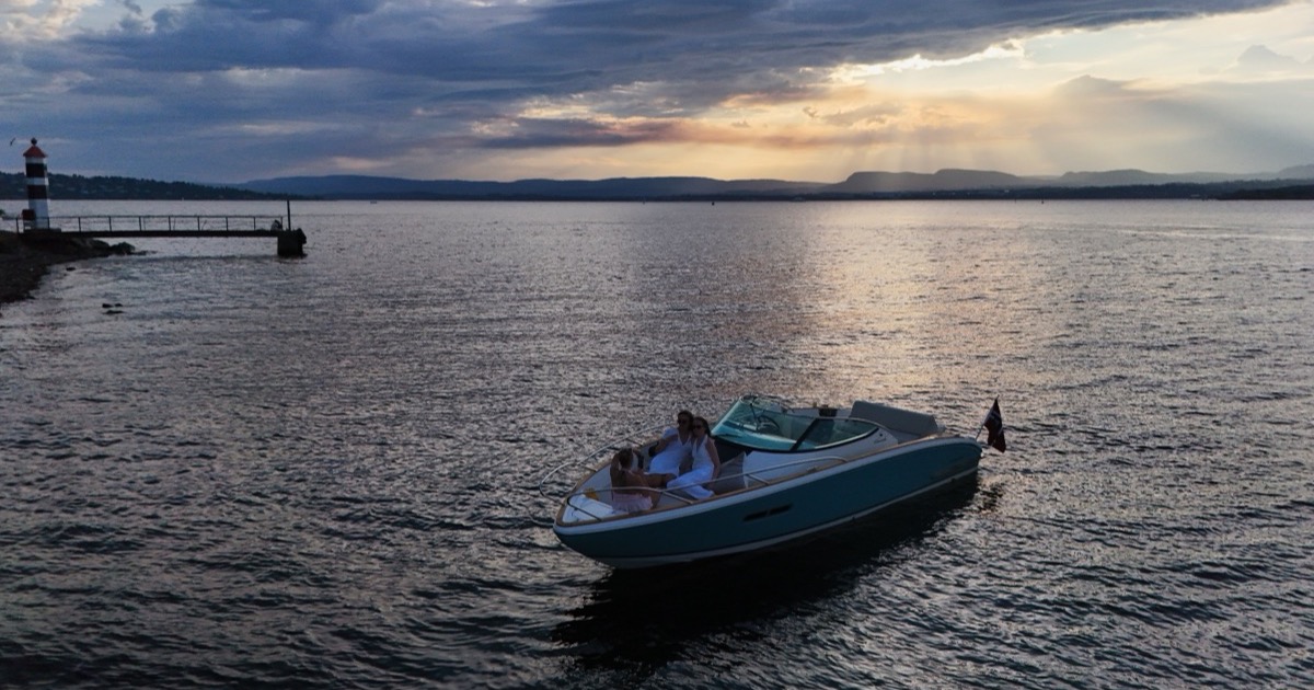 The boat at dusk near a lighthouse under a dramatic Nordic sky